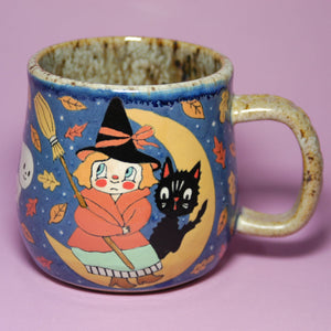 Ceramic mug with witch and black cat design on a purple background