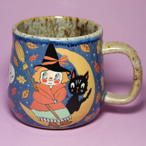 Ceramic mug with witch and black cat design on a purple background