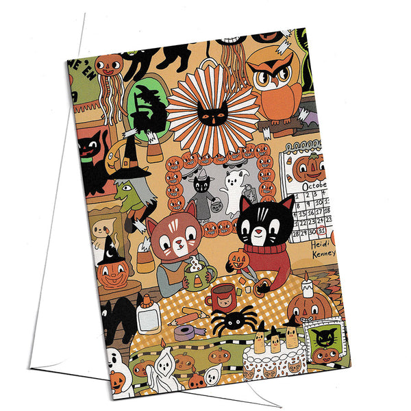 A Halloween-themed  card featuring a busy collage of illustrated cats, pumpkins, ghosts, a spider, and seasonal decor, shown against a plain white background with a white envelope behind it.