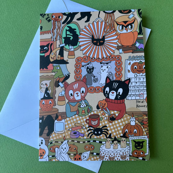 A Halloween-themed art print or card featuring a busy illustrated scene with pumpkins, ghosts, cats, owls, spiders, and a calendar, placed on top of a white envelope against a green background.