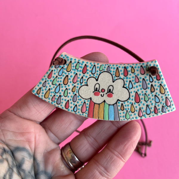 Hand holding a colorful cloud and rainbow design with a pink background