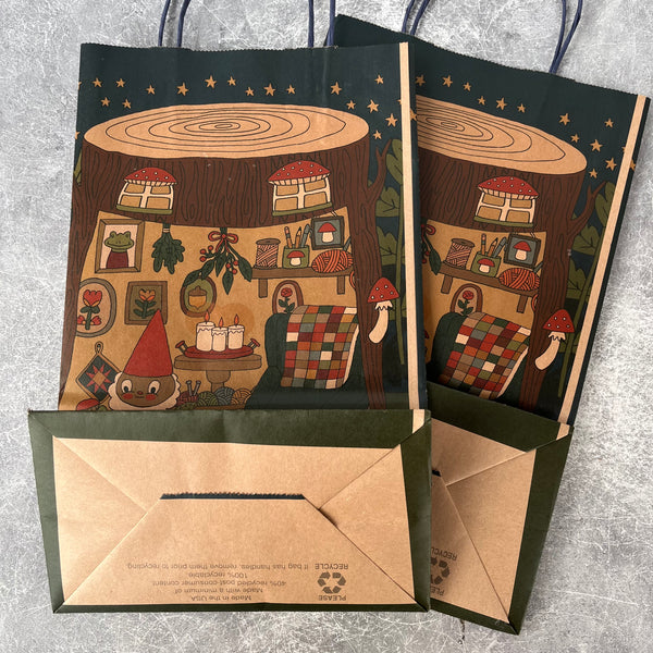 Two illustrated paper bags with a design of a gnome village on a gray surface.