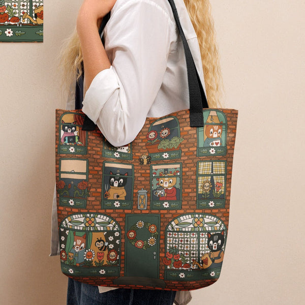 Woman holding a tote bag with a colorful pattern of an apartment building, standing next to a wall with a similar patterned painting.
