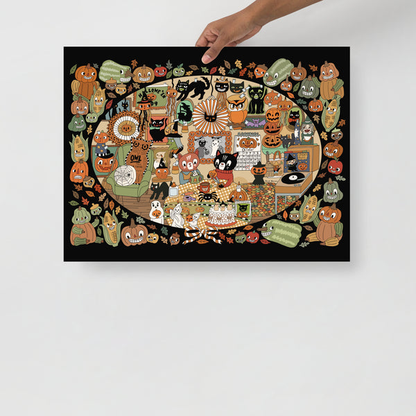 A rectangular wall art print or poster with a black background and a dense Halloween-themed illustration featuring many cartoon cats, pumpkins, leaves, and seasonal motifs, held up by a person's hand against a light gray wall.