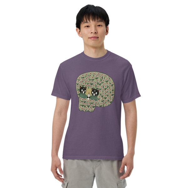 A man wearing a purple crewneck t-shirt with a large graphic of a skull made of green, beige, and black cat faces, paired with light gray cargo pants, against a plain white background.